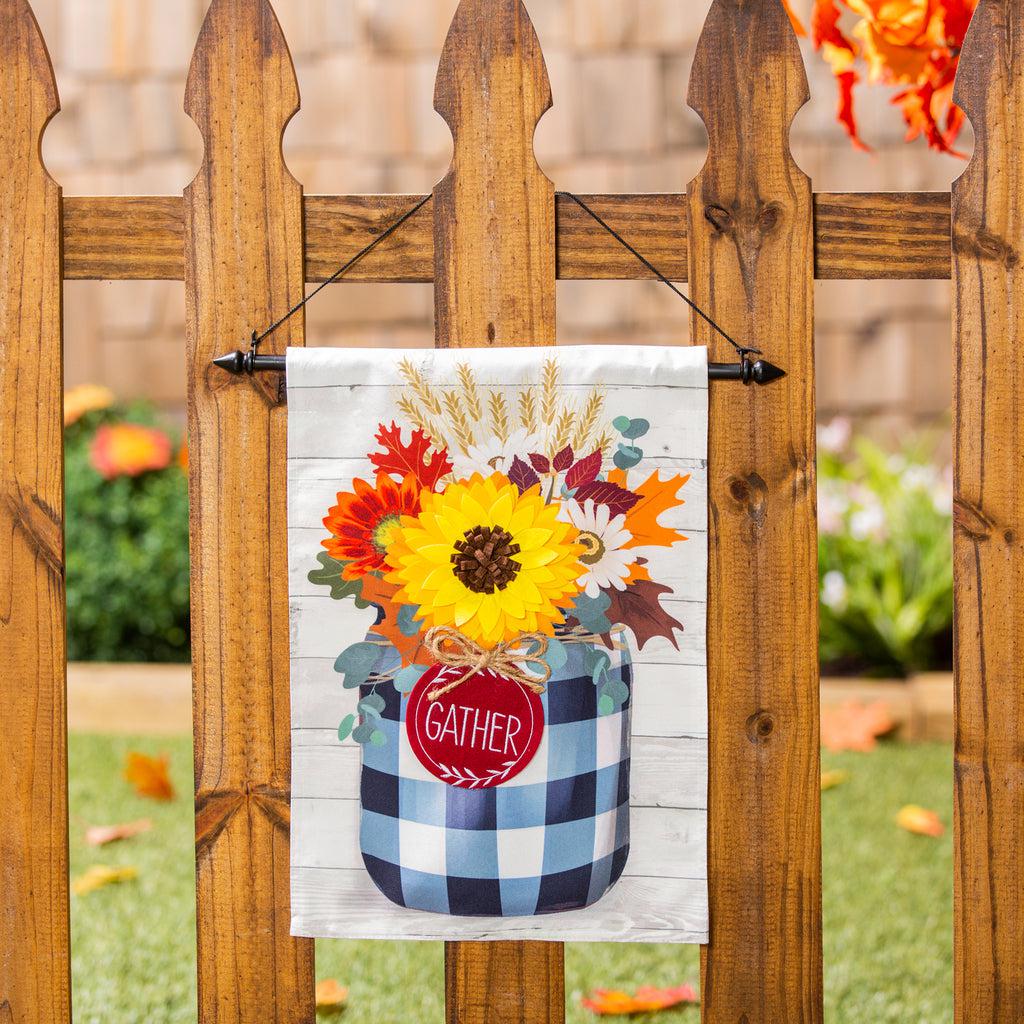 The Fall Check Mason Jar garden flag features an array of fall flowers in a black checked mason jar with a tag that says "Gather". 