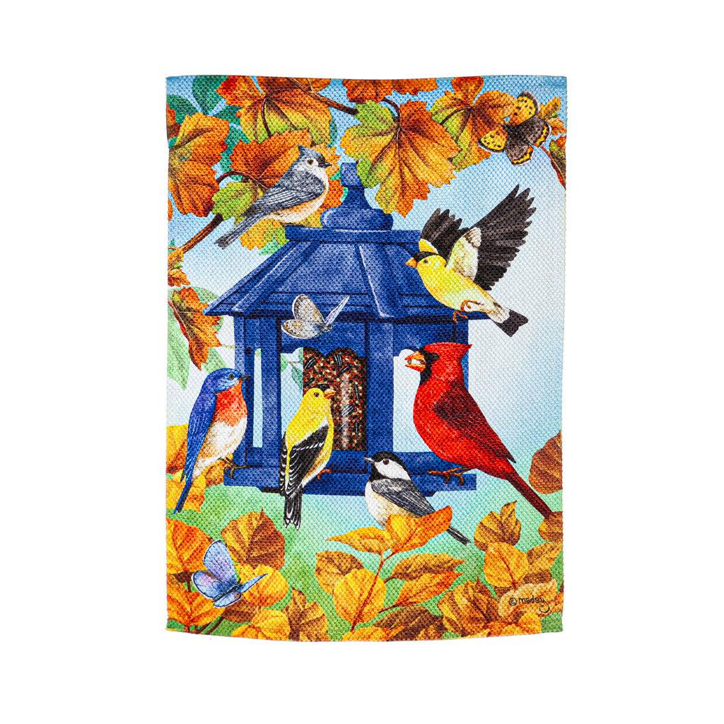 The Fall Feeder garden flag features a multitude of birds feasting from a blue bird feeder surrounded by fall leaves.