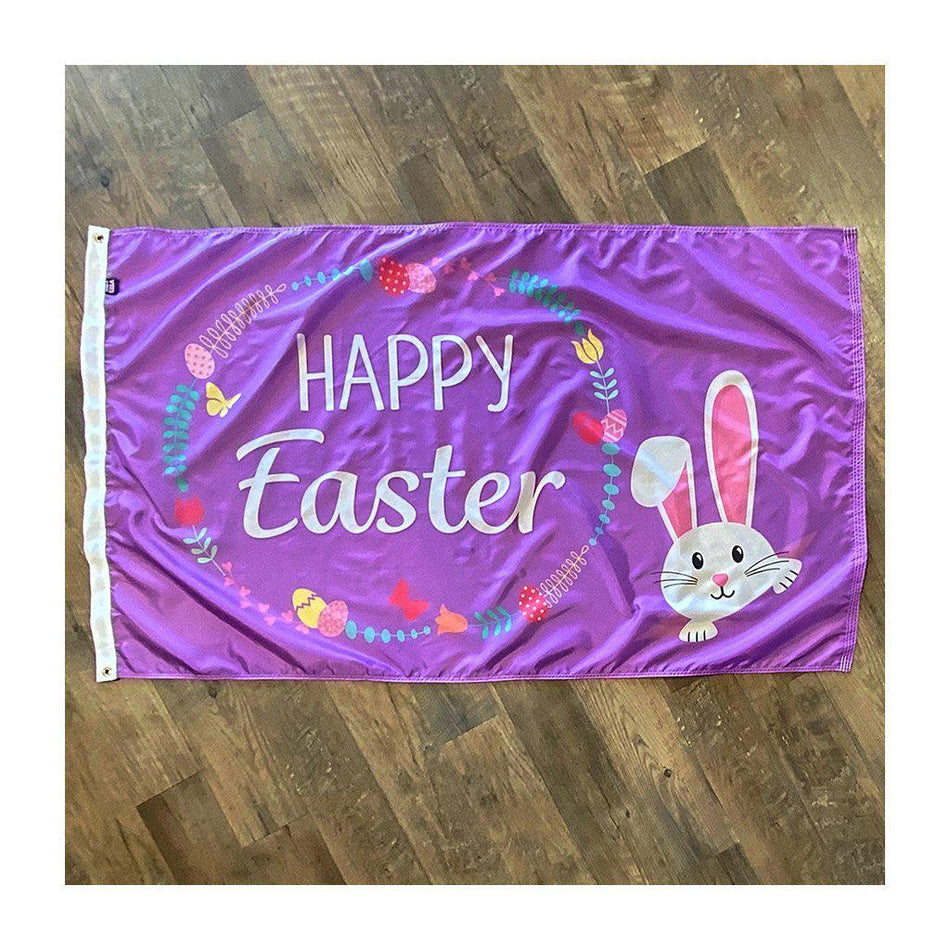 Our Happy Easter Wreath 3' x 5' flag features a cute bunny peeking out from the corner, eggs and flowers in a wreath design , and "Happy Easter" message on a purple background.