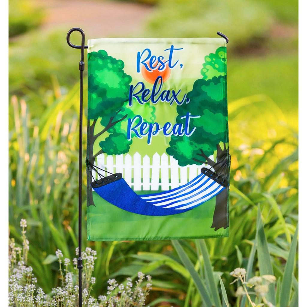 The Rest, Relax, Repeat Hammock garden flag features a blue and white striped hammock strung between two trees and the words "Rest, Relax, Repeat". 