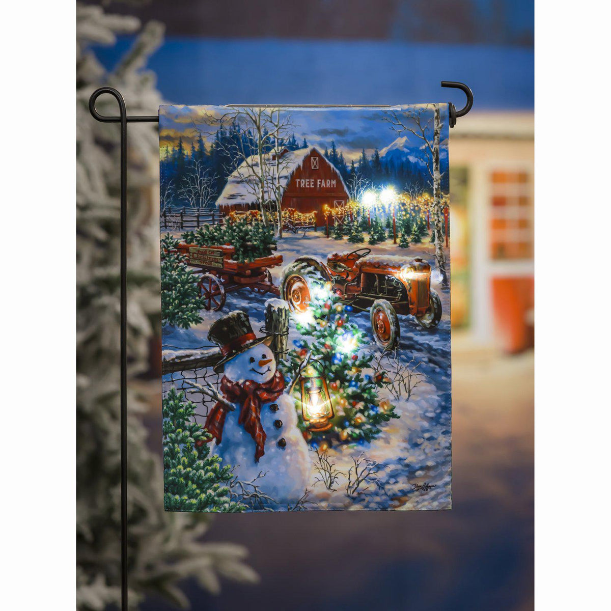 The Tree Farm Solar LED garden flag features a snowy Christmas tree farm complete with a tractor, wagon, barn, and snowman. 