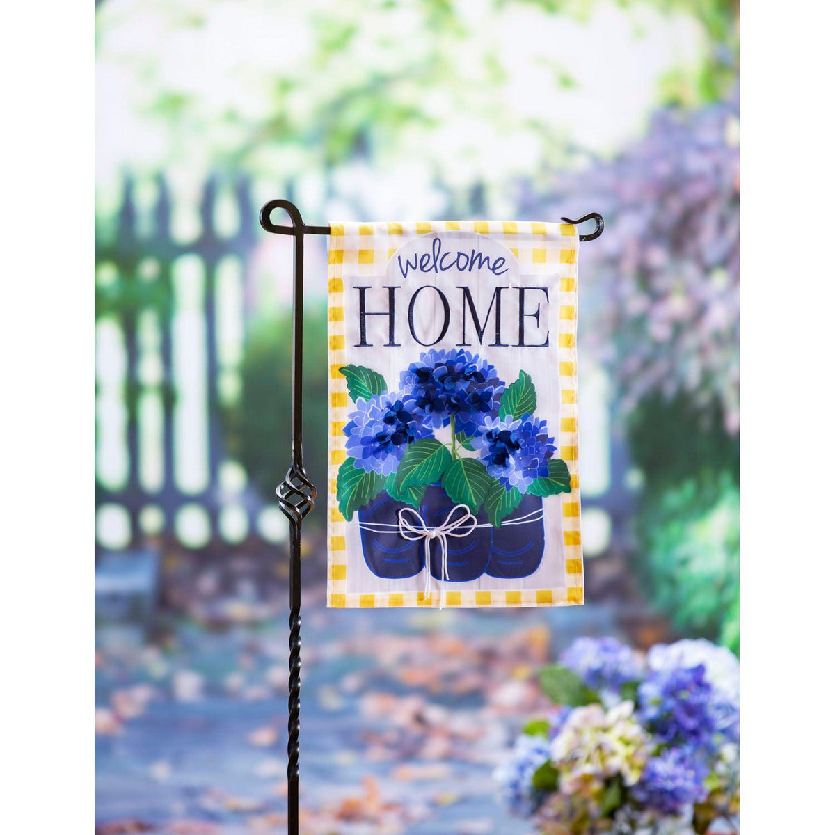 The Welcome Home Hydrangeas garden flag features vivid royal blue potted hydrangeas, a yellow checked border, and the words "Welcome Home" across the top of the flag.